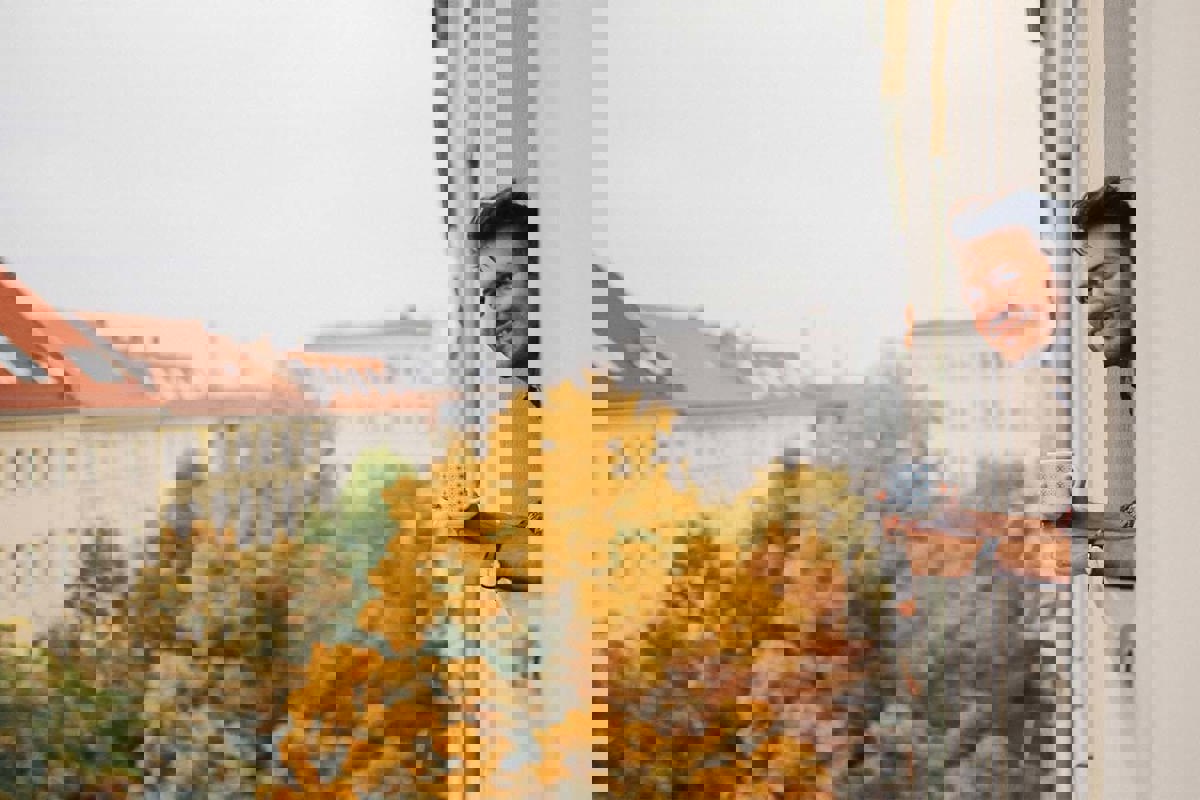 Man kigger ud af vindue i lejlighed med en kop kaffe i hånden